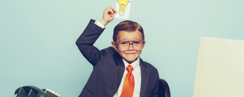 A boy wearing a tie and a shirt holding a picture of a lightbulb over his head