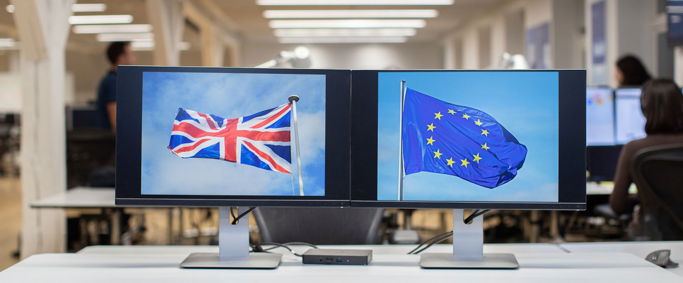Two computer monitors with the uk and eu flag on the screens
