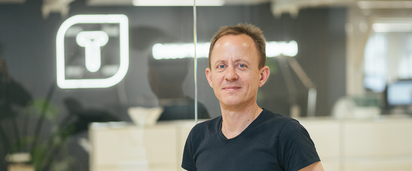 A man in a black shirt smiling in front of a window